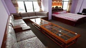 A room with a sofa, a bed, a glass-top coffee table, and a television. - MeroStay 165 HOTEL RI (Kathmandu)