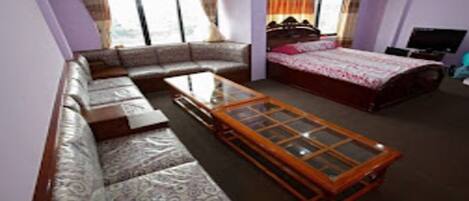A room with a sofa, a bed, a glass-top coffee table, and a television.