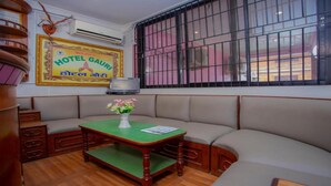 A hotel room with a green cushioned bench, a small table with a vase of flowers, and a large window with bars. - MeroStay 165 HOTEL RI (Kathmandu)