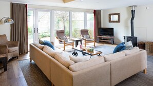 Een woonkamer met een bank, stoelen, een televisie, een open haard en een schuifpui naar buiten.