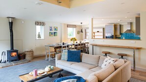 Een woonkamer met een bank, een salontafel, een open haard, een eethoek en een keuken met een fornuis.