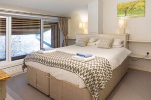 A bedroom with a large bed, a window with curtains, a bedside table, and a wall-mounted lamp. - Sleeps 14, 7 Bedrooms, 2 Dogs Welcome, No Smoking, Wood burner, Garden, Cot and Highchair,  Children (Cheltenham)
