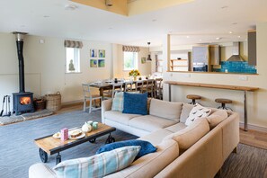 A living room with a sofa, a coffee table, a fireplace, a dining area, and a kitchen with a stove. - Sleeps 22, 11 Bedrooms, Dogs Welcome, No Smoking, Wood burner, Wi-Fi, Garden, Games Room (Cheltenham)