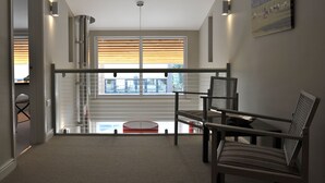 A spacious balcony with a glass railing, a seating area with chairs, and a view of a building with a balcony. - Modern Barn Conversion, 3 bedrooms (Cheltenham)
