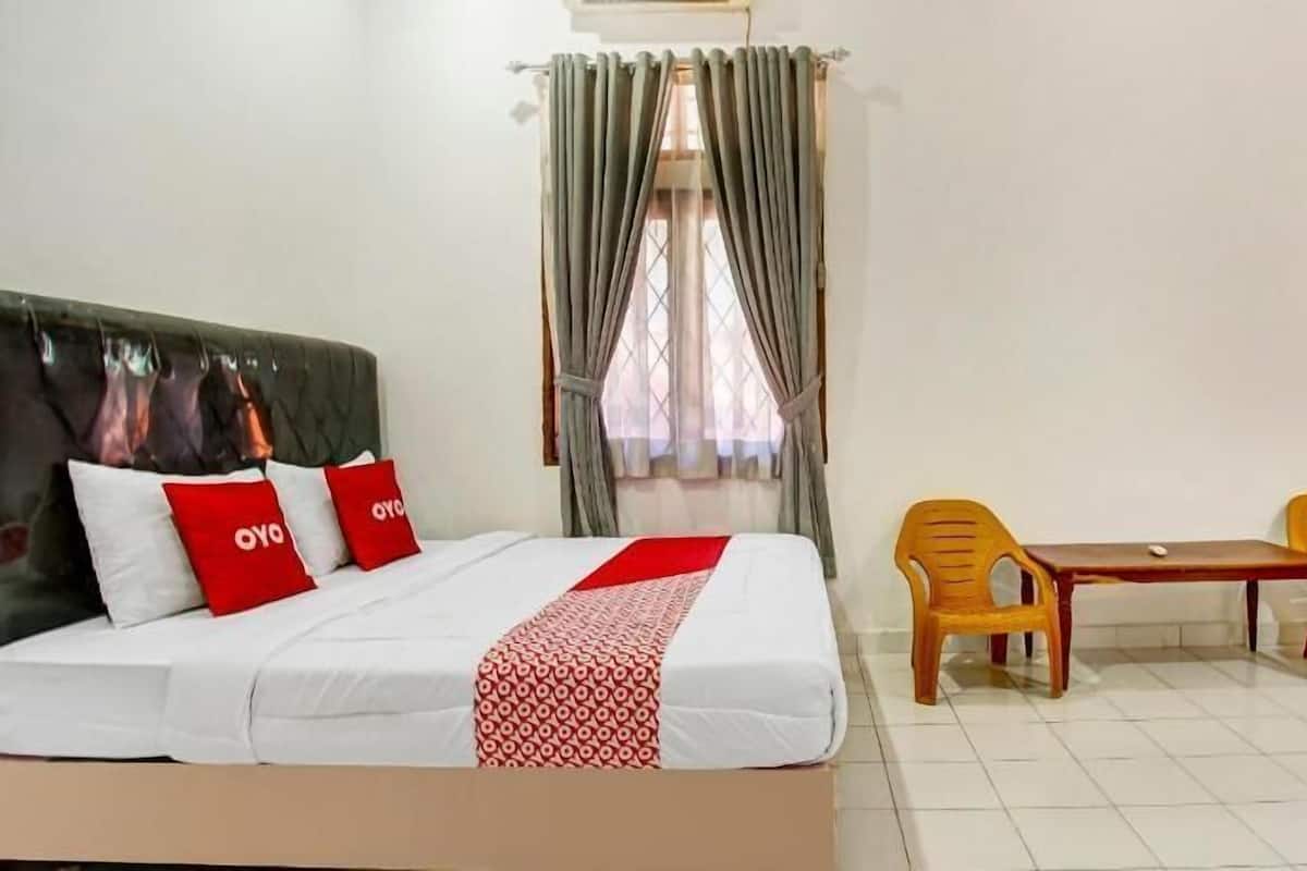 A hotel room with a bed, a window with curtains, a wooden table with two chairs, and a door.
