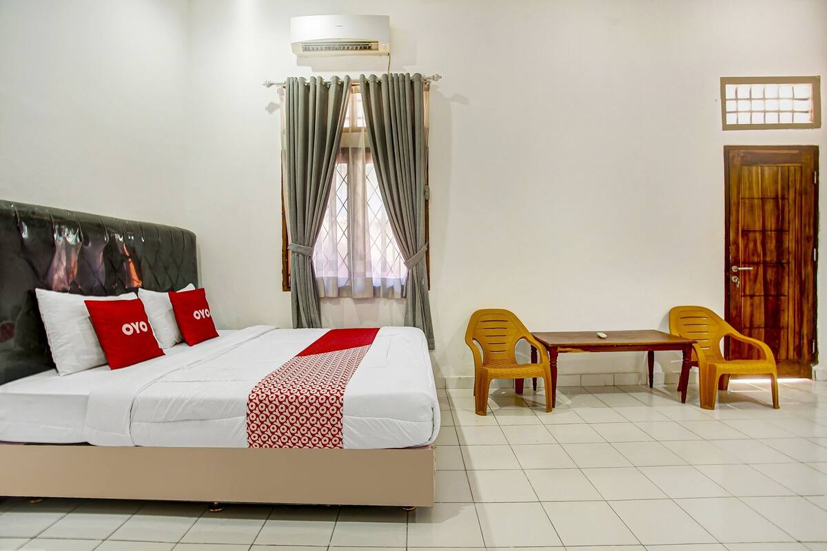 A hotel room with a bed, a table with chairs, an air conditioning unit, and a window with curtains.