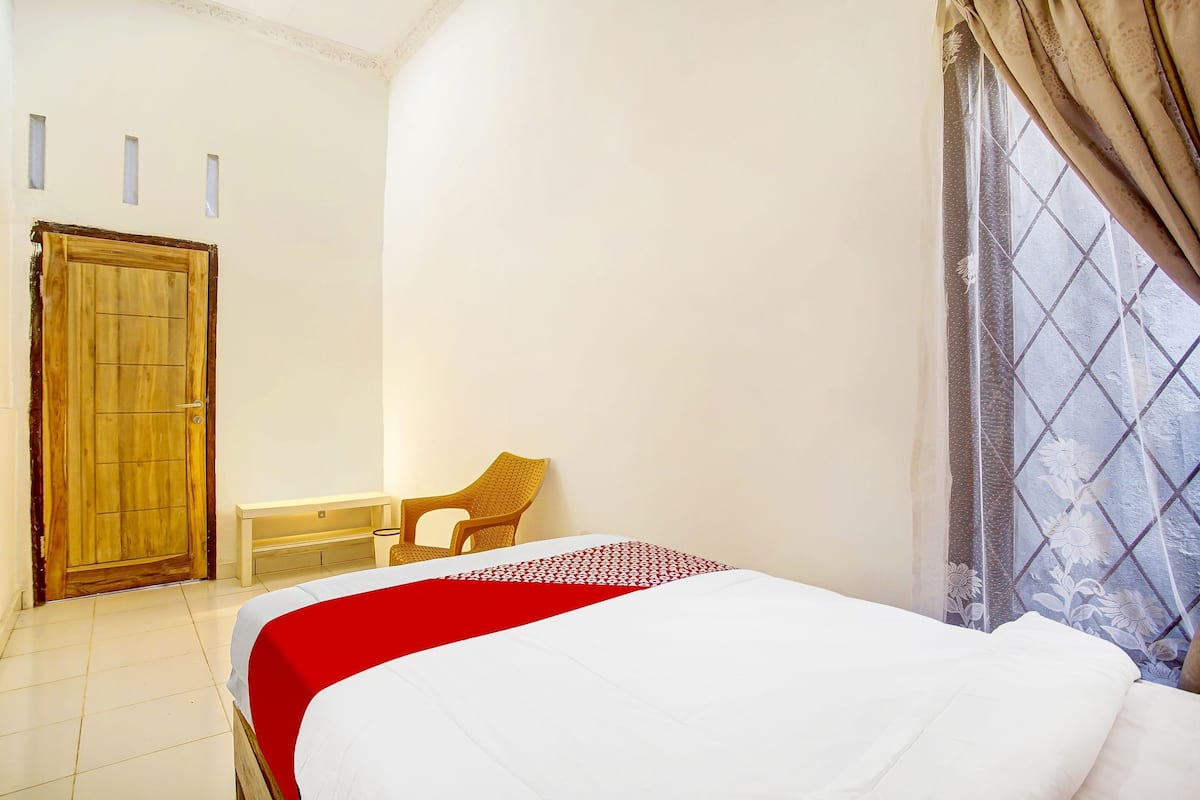 A bedroom with a bed, a wooden door, a bench, and a window with a curtain.