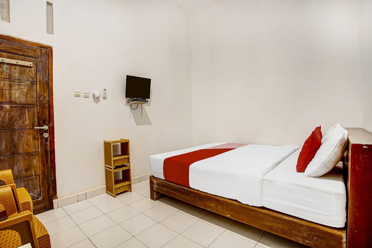 A bedroom with a wooden bed, a TV mounted on the wall, and a wooden shelf unit.