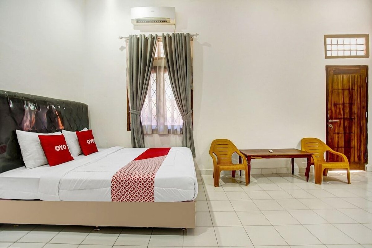 A hotel room with a bed, a table, two chairs, an air conditioner, and a window with curtains.