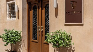 Fachada de edificio con una puerta doble de madera, dos plantas en macetas y un letrero que dice "LA TORRE DEL CASTELLI".