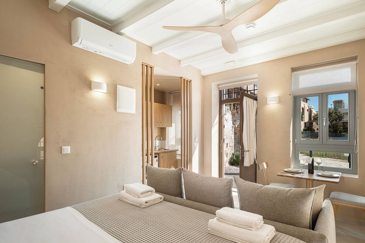 A hotel room with a bed, a ceiling fan, a window with a view, and a door.
