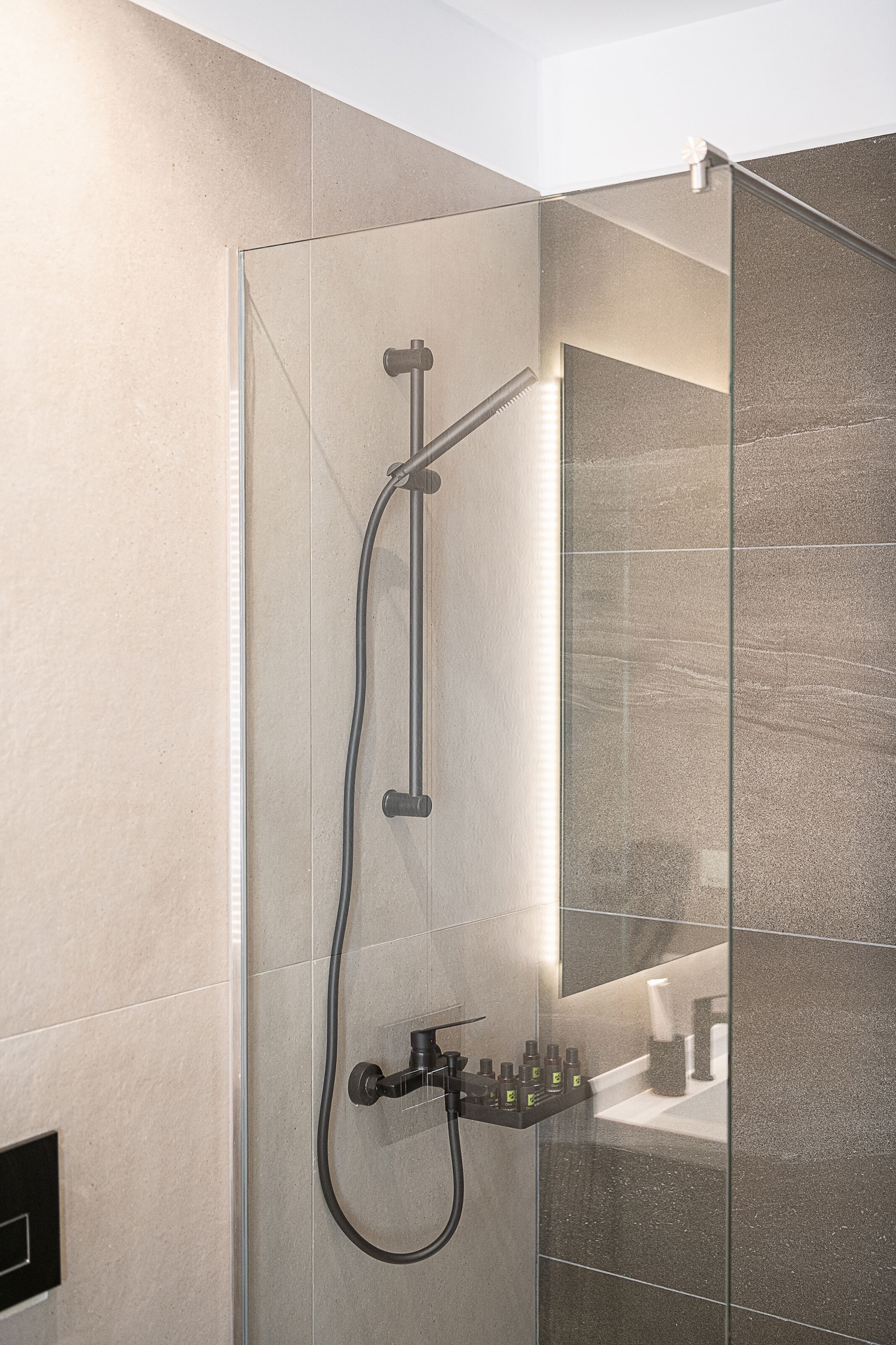 A modern shower with a glass enclosure, a handheld showerhead, and a wall-mounted faucet.