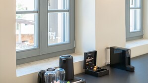 Una habitación con ventana, una bandeja con vasos y una cafetera, y una pequeña mesa.