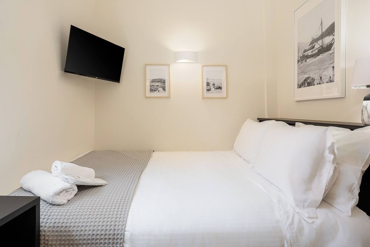 A hotel room with a bed, a flat-screen TV mounted on the wall, and two framed pictures on the wall.