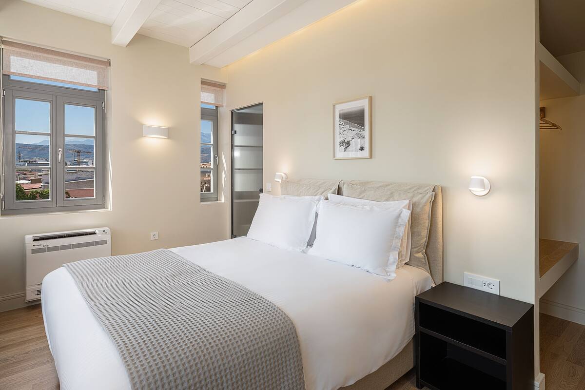 A bedroom with a bed, bedside table, and a view of the outside.