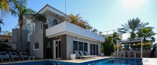 A modern two-story house with a swimming pool, outdoor seating, and a pergola.