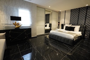 A modern bedroom with a large bed, a vanity with a mirror, and a black marble floor.