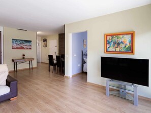 Uma sala de estar com televisão de tela plana, uma área de jantar com cadeiras e um quadro na parede.