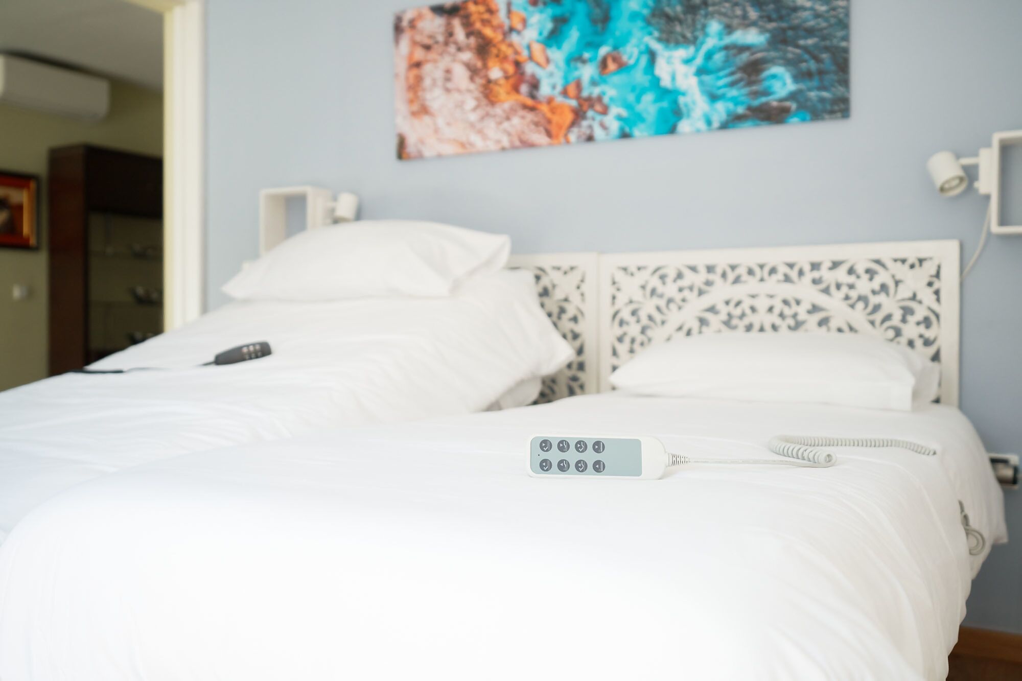 Una cama bien hecha con sábanas blancas, un control remoto y una almohada blanca.