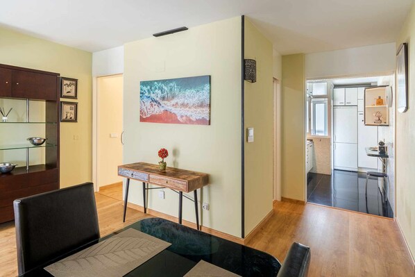 Uma sala de estar moderna com área de jantar, cozinha ao fundo e um grande quadro abstrato na parede.
