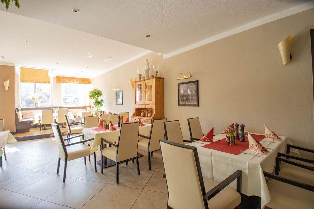 Un comedor con varias mesas dispuestas para comensales, un aparador de madera con adornos y un cuadro en la pared.