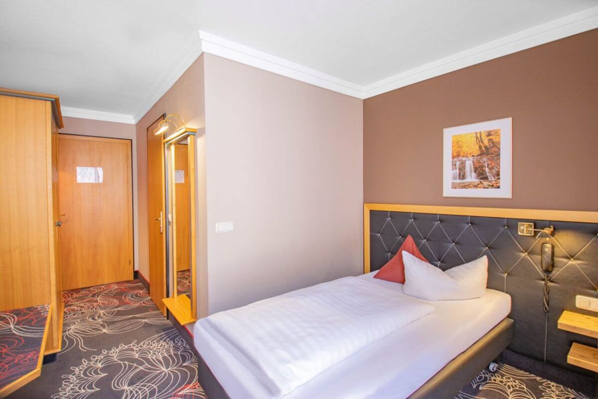 A hotel room with a bed, a bedside telephone, a mirror, and a door.