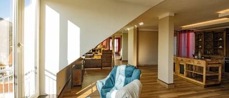 Un loft espacioso con techo alto, un sillón azul, una mesa de comedor de madera y vistas de la ciudad a través de grandes ventanales.