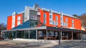A modern building with a red facade, large windows, and a glass extension. - Hotel Tanne (Ilmenau)