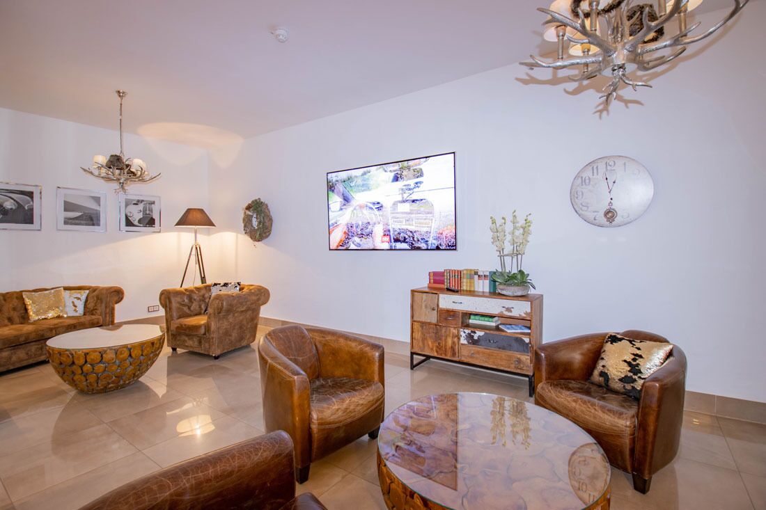 A modern living room with a sofa set, two armchairs, a coffee table, a sideboard, and a wall-mounted TV.