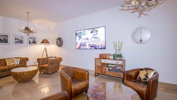 A modern living room with a sofa set, two armchairs, a coffee table, a sideboard, and a wall-mounted TV.
