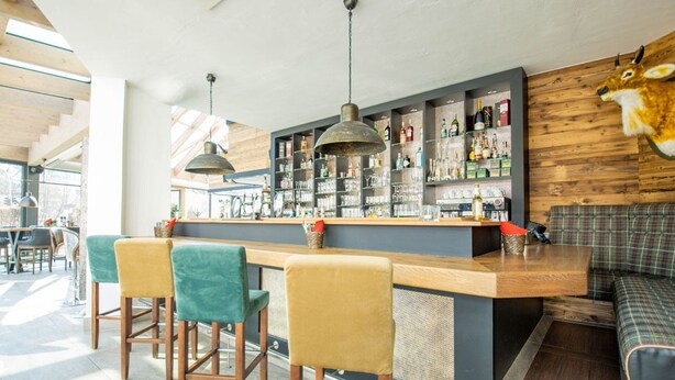 A bar area with a wooden counter, stools, and shelves stocked with bottles and glasses. - Hotel Tanne (Ilmenau)