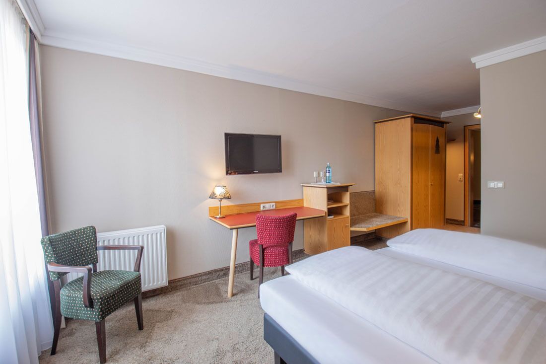 A hotel room with a bed, a desk, a chair, a television, and a wardrobe.