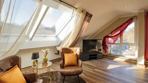 A modern living room with a leather armchair, a small round table, and a flat-screen TV. - Hotel Tanne (Ilmenau)