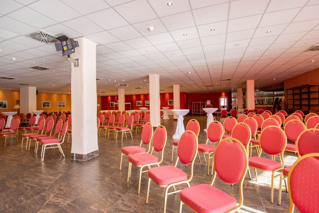 A large hall with rows of red chairs and white tables, likely for events or conferences.