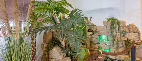 A room with a rock wall, green plants, and a rope barrier.