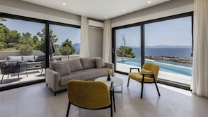 A modern living room with a sofa, two chairs, a coffee table, and large windows offering a view of a pool and the sea. - Villa Luce (Pijavicino)