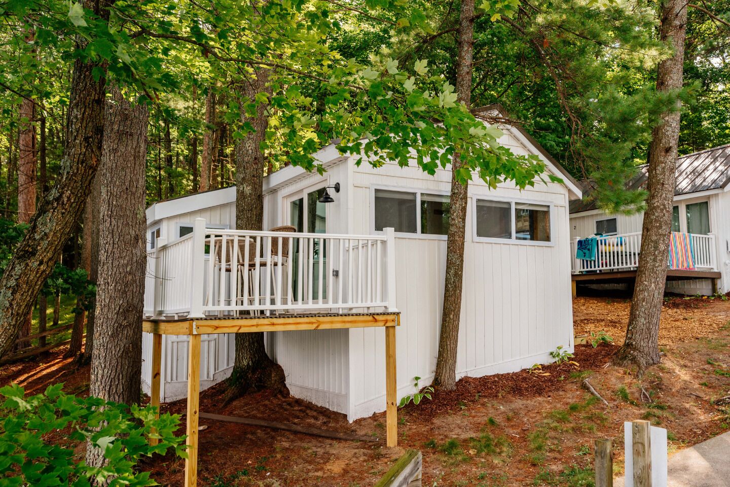 Une cabane dotée d’une terrasse et d’un petit porche, entourée d’arbres.
