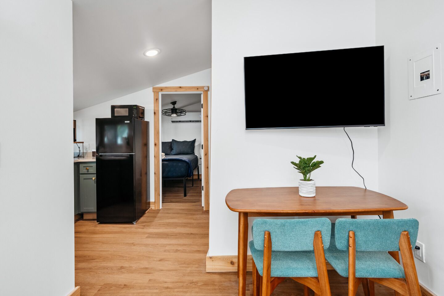 A compact living space with a kitchenette, a dining area with a table and chairs, and a TV mounted on the wall.