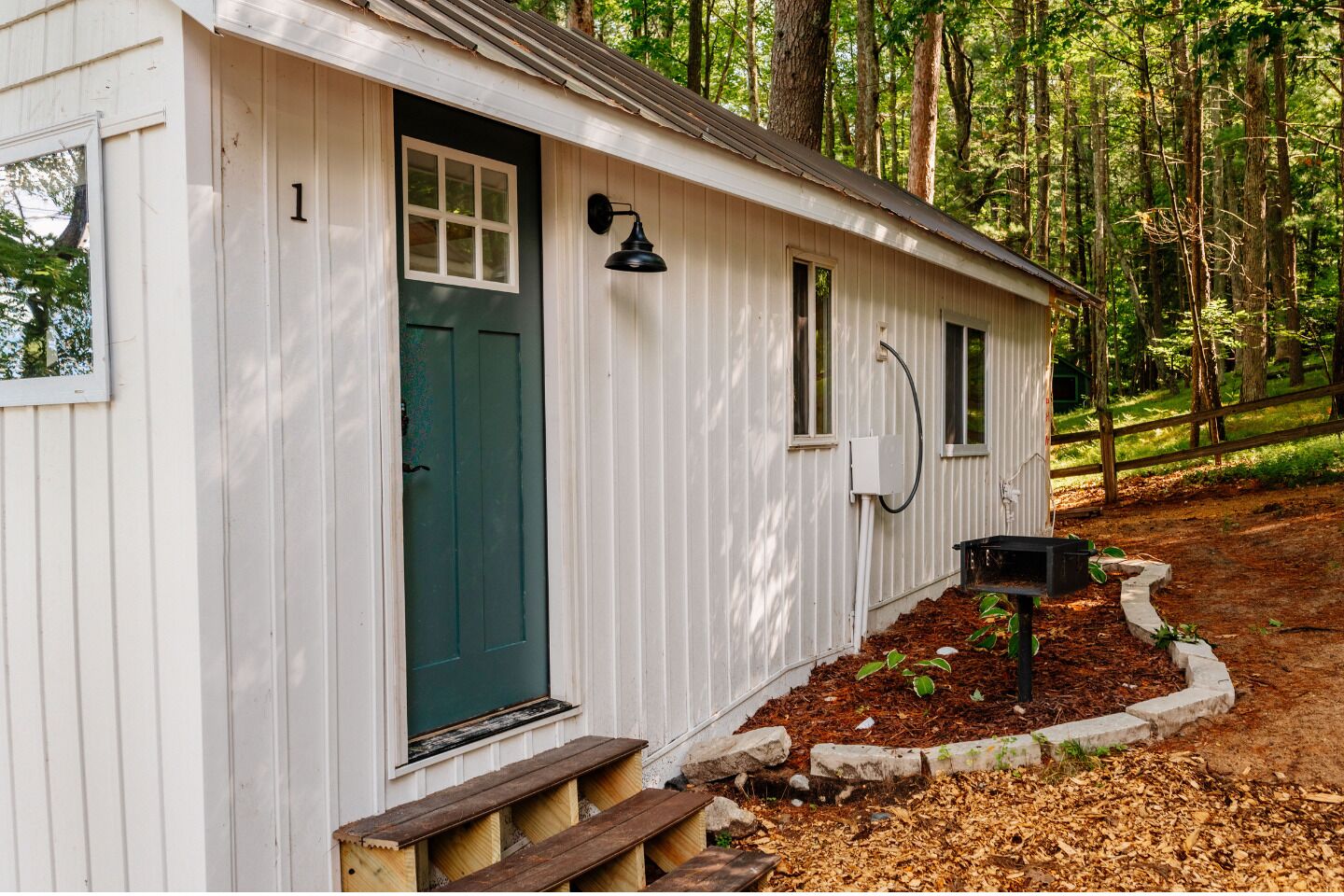 Une petite cabane à un seul étage, avec une porte verte, une boîte aux lettres et un banc en bois à l’extérieur.