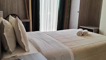 A hotel room with a bed, a desk with a telephone, a wardrobe, and an air conditioning unit.