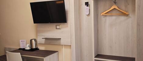 Habitación de hotel con cama, escritorio con silla, televisor y armario con perchero.