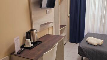 Ein Hotelzimmer mit Schreibtisch, einem Bett, einem an der Wand befestigten Fernseher, einer Kaffeemaschine und einer Fernbedienung auf dem Schreibtisch.