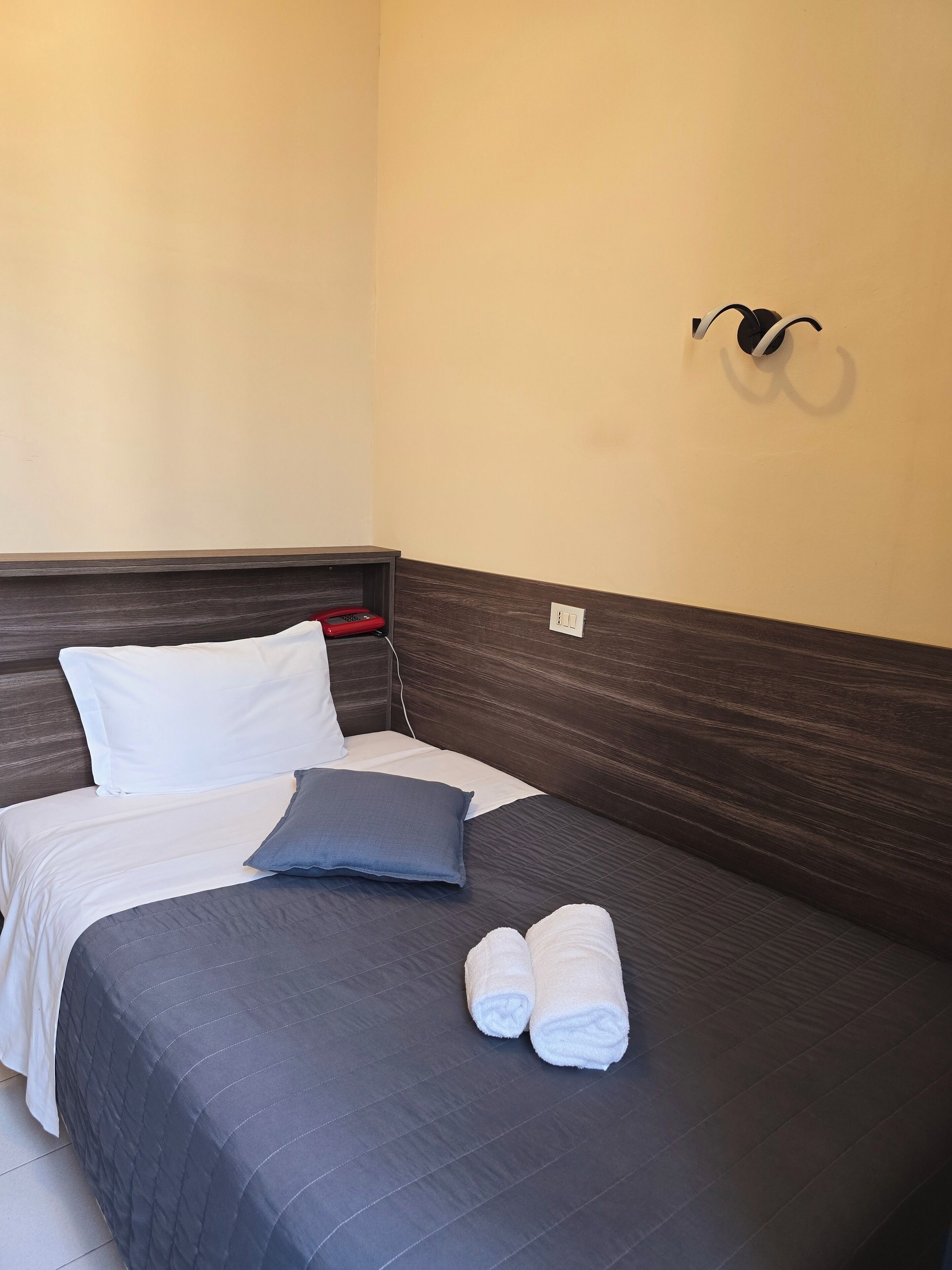 A neatly made bed with a dark blue bedspread, white pillows, and two rolled towels.
