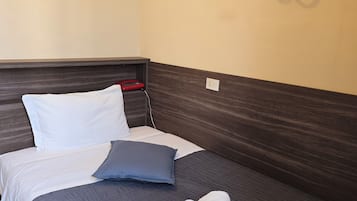 Un lit bien fait, recouvert d’une couvre-lit bleu foncé, avec des oreillers blancs et deux serviettes enroulées.