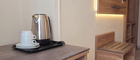 A kitchenette with a coffee maker, a small trash bin, and a wooden cabinet with a television mounted above.
