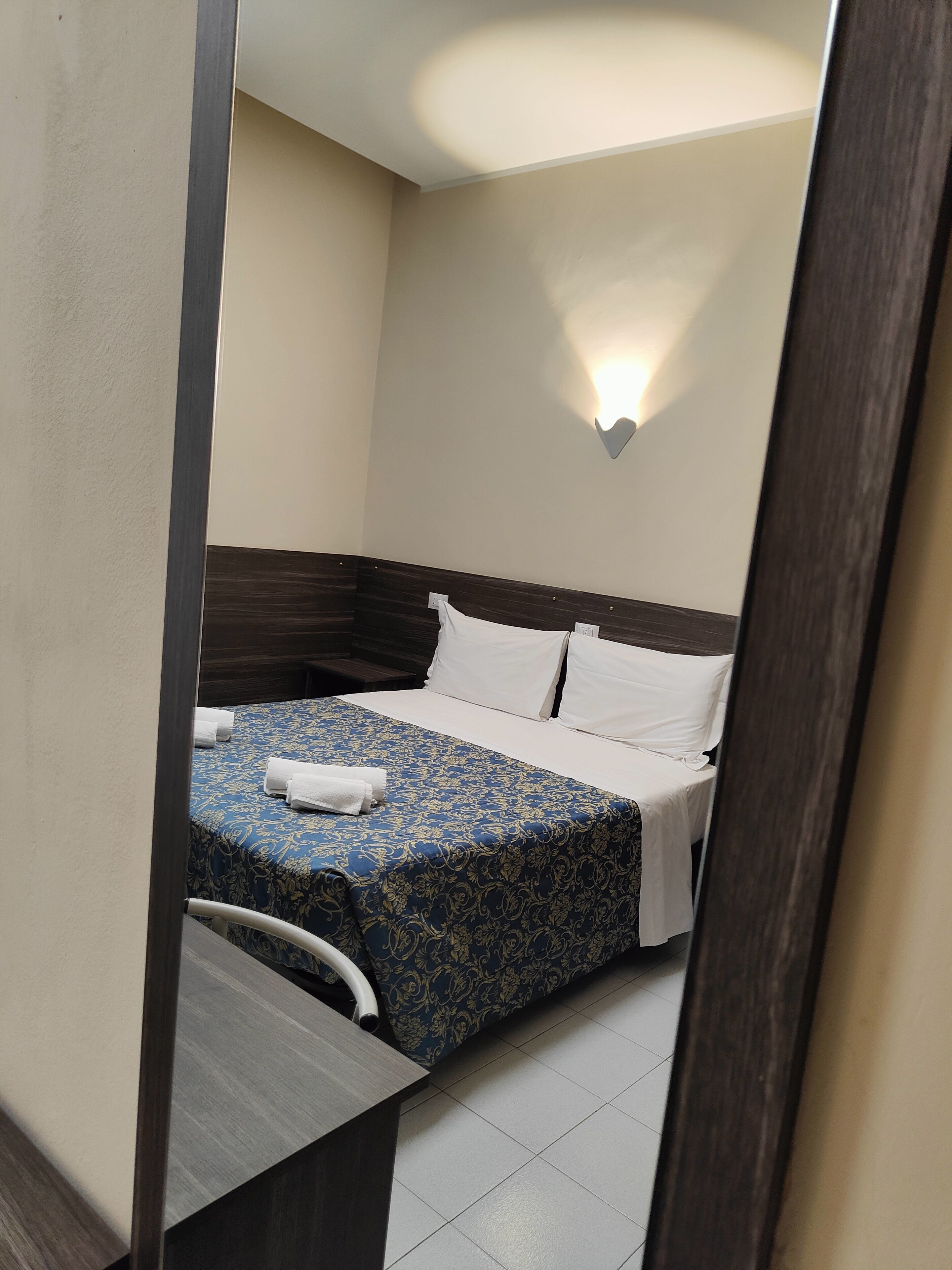 Una habitación de hotel con una cama, una mesita de noche y una lámpara fijada a la pared.