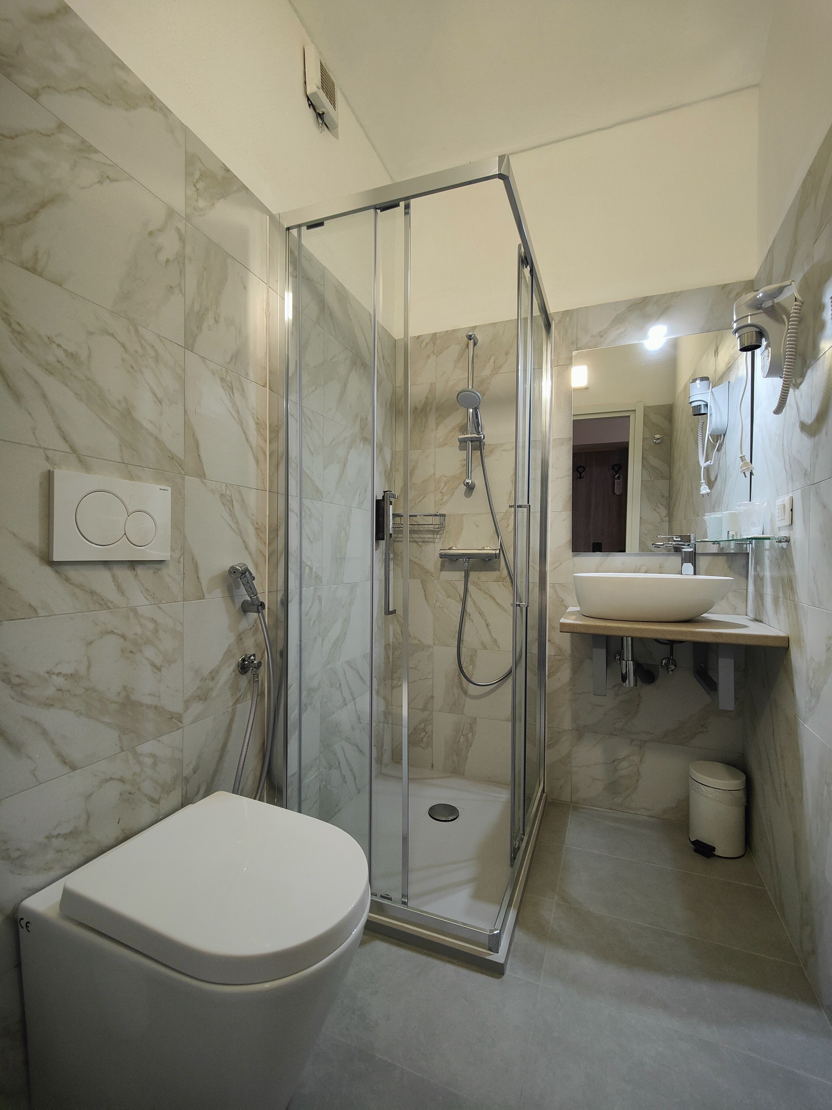 Un bagno moderno con doccia vetrata, un water bianco, un lavabo con piano in marmo e uno specchio sopra il lavabo.