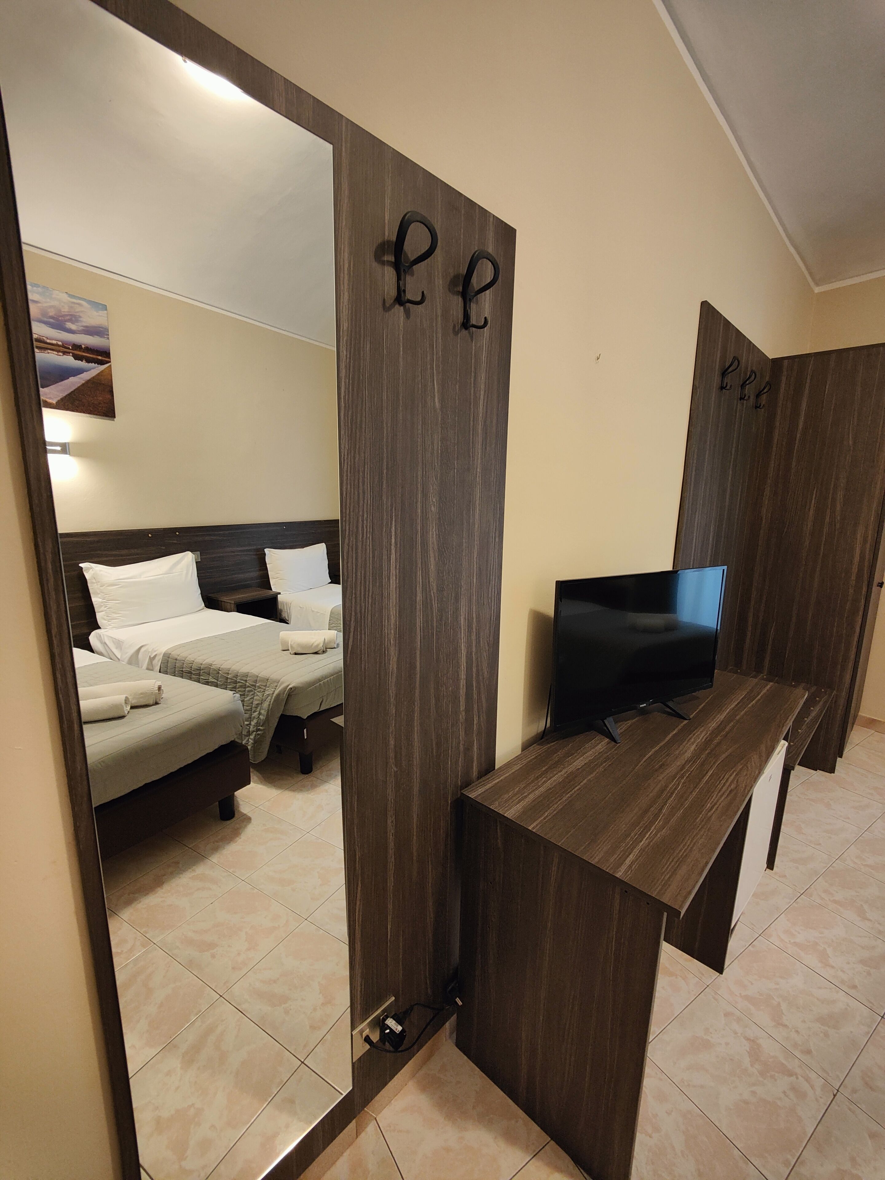 Une chambre d’hôtel avec deux lits, une télévision et un miroir qui reflète la pièce.