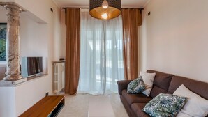 Un soggiorno moderno con un divano marrone, un pouf bianco e una televisione su una colonna di marmo.