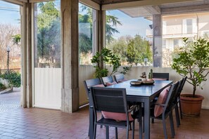 Eine überdachte Terrasse mit Tisch und Stühlen, Blumentöpfen und Blick auf eine Wohngegend.
